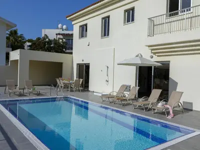 a swimming pool with chairs and an umbrella next to a building at Protaras Villa Theodora 1 in Protaras