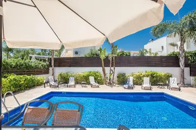 a swimming pool with chairs and an umbrella at Protaras Villa Theodora 27 in Protaras
