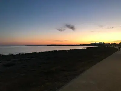 a sunset at the beach with a person walking on a sidewalk at My Holiday in Ayia Napa