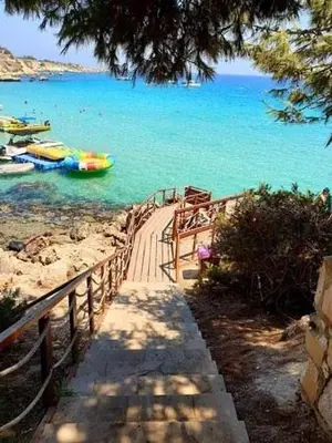 a wooden walkway leading to a beach with boats in the water at My Holiday in Ayia Napa