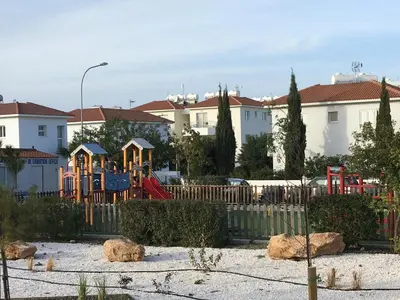 a park with a playground with a fence and houses at AP10 Mythical Sands in Protaras