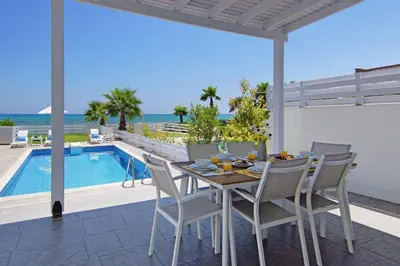 a dining table and chairs on a patio with a pool at Villa Ivory - Seafront in Ayia Napa