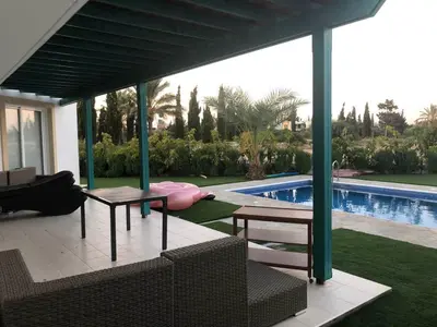 a covered patio with a table and chairs next to a swimming pool at Oasi Rejuve Poseidon in Meneou