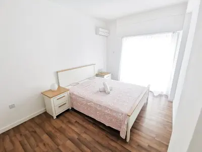 a white bedroom with a bed and a wooden floor at Island Time Holiday Apartment in Larnaka