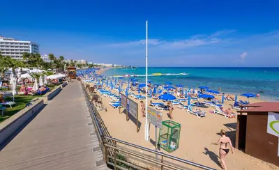 a beach with blue chairs and people on the beach at Olivine Waves in Protaras