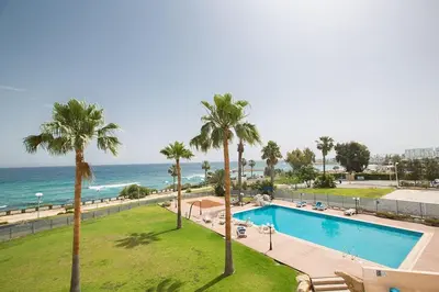 a swimming pool with palm trees and the ocean at Apt Lasonos Asimi - Luxury 3 Bedroom Protaras Apartment - Communal Pool in Protaras