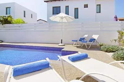 a pool with chairs and an umbrella next to a building at Villa Greta in Protaras