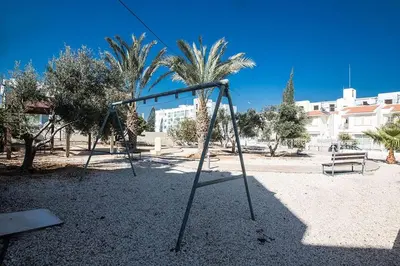a swing set in a park with trees and buildings at Villa Dafnis Platina - Lovely 4 Bedroom Protaras Villa With Private Pool in Protaras
