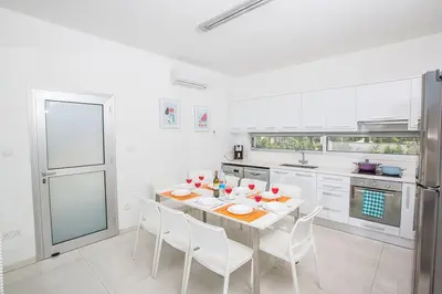 a white kitchen with a table and white chairs at Villa Ochosto Selene - Stunning 5 Bedroom Protaras Villa With Private Pool in Protaras