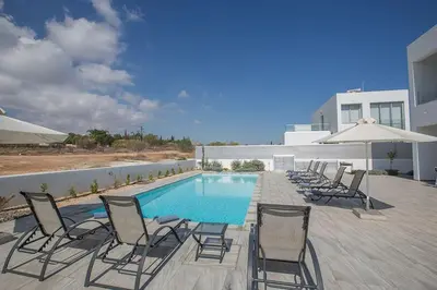 a pool with chairs and umbrellas next to a building at Villa Ochosto Loux - Fabulous 5 Bedroom Protaras Villa With Private Pool in Protaras