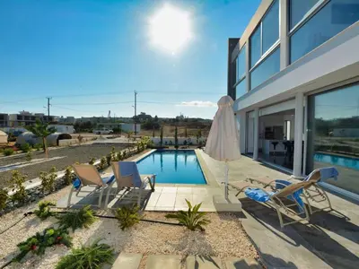 a backyard with a swimming pool and chairs and a building at Villa Manta Chrysos - Brand New Luxury 3 Bedroom Protaras Villa in Protaras