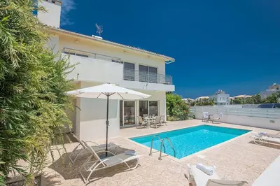 a swimming pool with an umbrella and chairs and a house at Central Protaras Villa 3 Bedrooms Private Pool Villa Dafnis Morfi in Protaras