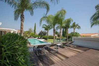 a deck with chairs and a swimming pool with palm trees at Villa Protaras Sunshine, Stylish 4Bdr Villa With Pool, Close To Fig Tree in Protaras