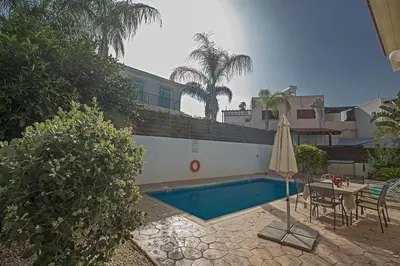 a swimming pool with a table and an umbrella at Villa Dafnis Sunshine - Modern 3 Bedroom Central Protaras Villa With Pool in Protaras