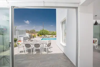 a glass door leading to a patio with a table and chairs at Villa Ochosto Helios - Beautiful 5 Bedroom Protaras Villa - Walking Distance in Protaras
