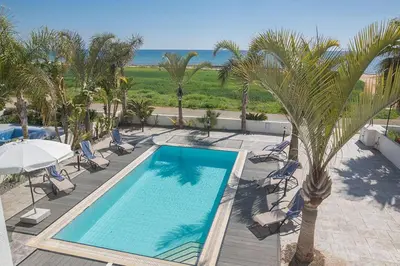 a swimming pool with chairs and palm trees and the ocean at Villa Adaman - Stunning 3 Bedroom Seafront Villa With Pool - Close To The Beach in Ayia Napa