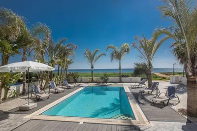 a swimming pool with chairs and palm trees and the ocean at Villa Adaman - Stunning 3 Bedroom Seafront Villa With Pool - Close To The Beach in Ayia Napa