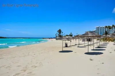 a row of umbrellas on a beach with the ocean at Nissi 3 Pool Access Garden Apartment in Ayia Napa