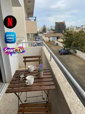 a wooden table on a balcony with cups and flowers at Larnaca Comfort Rooms With Smart TV & Netflix in Larnaka
