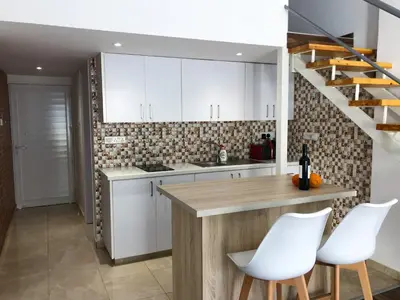 a kitchen with white cabinets and a counter with white chairs at Cozy Loft Apartment in Ayia Napa