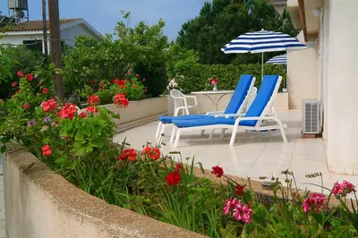 two chairs and an umbrella on a patio with flowers at Sunbay Apartments in Pyla
