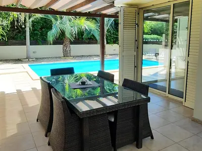a dining table and chairs with a pool in the background at Villa Larnaca Bay Resort in Voroklini