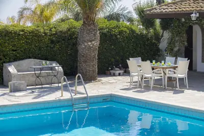 a pool with a table and chairs next to a palm tree at Protaras Villa Mazeri in Protaras