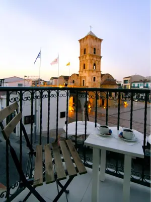 a table and chairs on a balcony with a clock tower at Hotel Opera in Larnaka