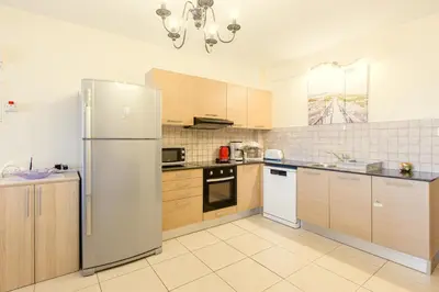 a kitchen with wooden cabinets and a stainless steel refrigerator at NISSI BEACH POOL VIEW APARTMENT FREE WIFI in Ayia Napa