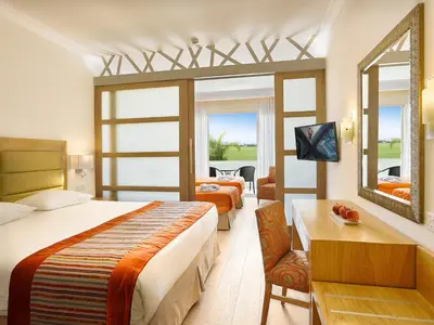 a bedroom with two beds and a desk and a mirror at Olympic Lagoon Resort Ayia Napa in Ayia Napa