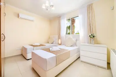 a white bedroom with two beds and a window at Royal Beachfront Villa in Protaras