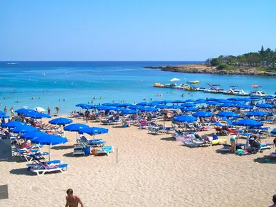 a beach with blue umbrellas and people on the beach at A209 Coralli Spa, Cyprus - Med View Studio in Protaras