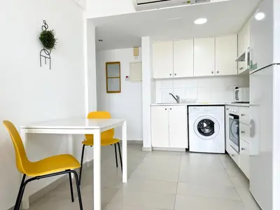 a white kitchen with a white table and yellow chairs at Lovely Studio Ayia Napa in Ayia Napa