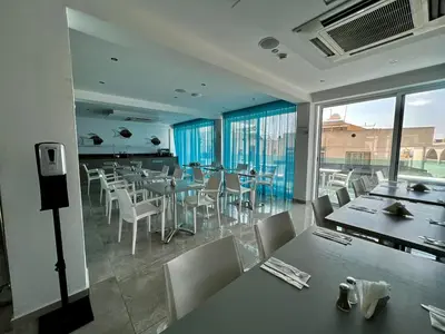 a dining room with tables and chairs and windows at Sunny Blue Hotel in Ayia Napa