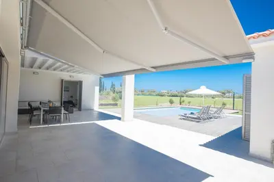 a white patio with a pool and a table and chairs at Leda Villa in Protaras