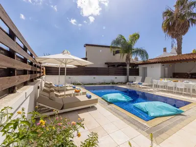 a pool with chairs and an umbrella next to a house at Villa Eftihia in Protaras