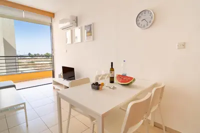 a white dining room with a white table and a clock at Mirabella Mackenzie 1 Bedroom Flat Near the Sea in Larnaka
