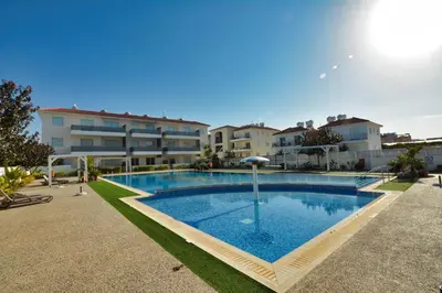 a swimming pool with an umbrella in front of some buildings at SunnyVillas: NEW Studio SPA & GYM in Kapparis in Protaras