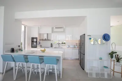 a white kitchen with blue chairs and a table at Villa Olivine Pearl 3 in Protaras