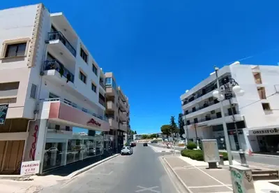 a street with two buildings and a car on the road at Mimi's Sunny Beach Apartment in Larnaka