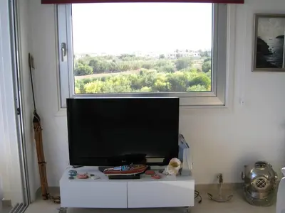 a flat screen tv sitting on a white stand in front of a window at Trident Beach Apartment in Protaras