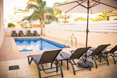 a pool with chairs and a table and an umbrella at Villa Alba, Luxury 4 BDRM Villa with Heated Pool in Protaras