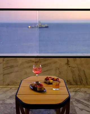 a table with a glass of wine and food on it at The Icon Limassol in Limassol