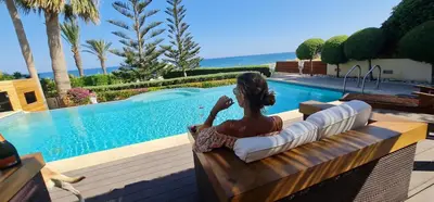 a woman sitting on a bench next to a swimming pool at Villa del Mar Heated pool in Mazotos