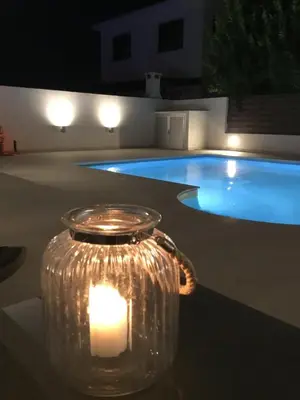 a candle in a glass jar next to a swimming pool at night at Katikies Grand in Pissouri
