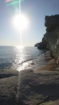 a beach with the sun shining on the water at Katikies Grand in Pissouri