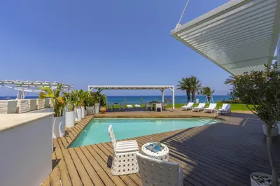 a swimming pool with chairs and the ocean in the background at Beachfront Dream Villa in Protaras