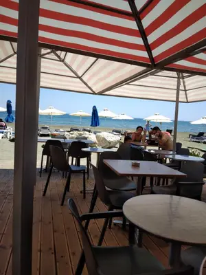 two people sitting at tables under an umbrella on the beach at MERSINERA Paradise Garden NOAH HOUSE in Kivisil