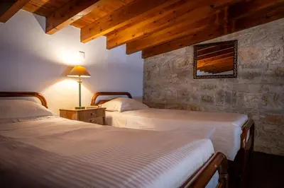 a bedroom with two beds and a stone wall at Oinoessa Traditional Boutique Guest Houses in Lofou