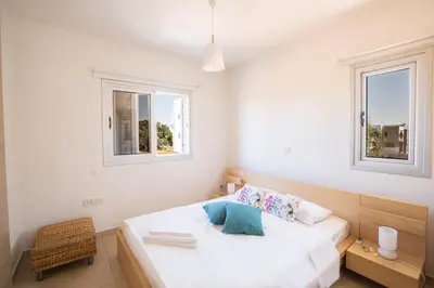 a white bedroom with a bed and two windows at Kalamies Family Villa in Protaras